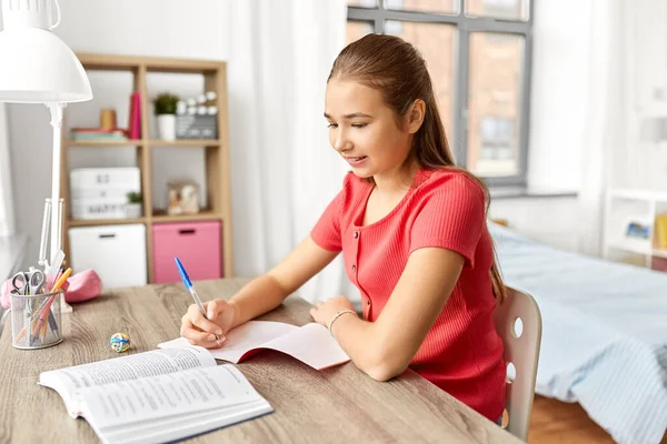 Student flicka med bok skriva till anteckningsbok hemma — Stockfoto