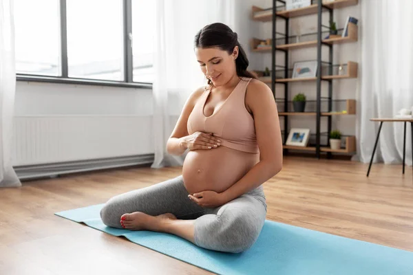 Happy pregnant woman sitting on yoga mat at home — Stock Photo, Image