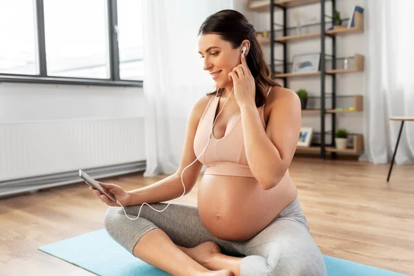 Schwangere mit Kopfhörern beim Yoga zu Hause — Stockfoto