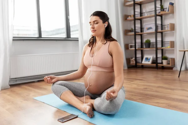 Mujer embarazada con auriculares haciendo yoga en casa — Foto de Stock