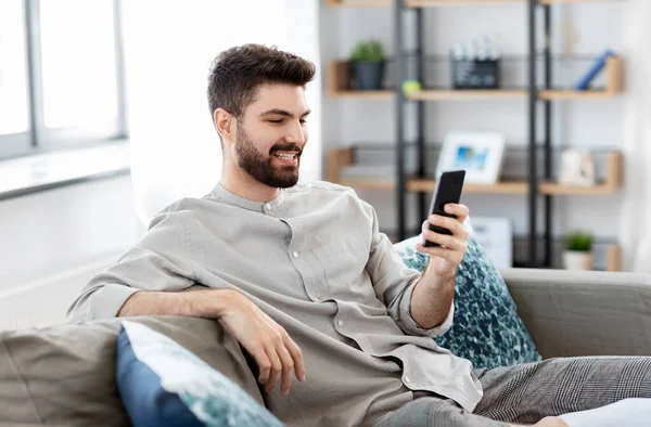 Šťastný usmívající se mladý muž s chytrým telefonem doma — Stock fotografie