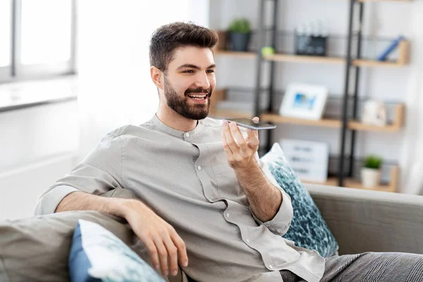 En lykkelig mann med smarttelefon som spiller inn stemme hjemme – stockfoto