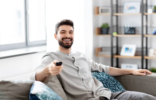 En glad mann med fjernkontroll som ser på tv hjemme – stockfoto