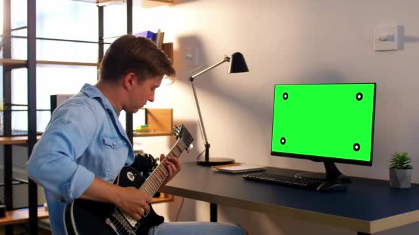 Ung man med dator spelar gitarr hemma — Stockvideo