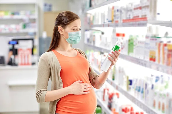 Mulher grávida em máscara escolhendo loção na farmácia — Fotografia de Stock