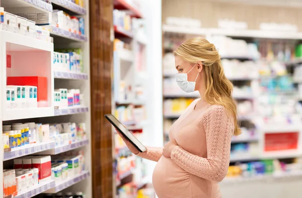 Mujer embarazada con máscara y tableta pc en la farmacia —  Fotos de Stock