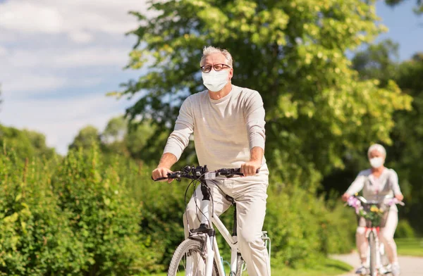 Senior par i masker ridning cyklar i parken — Stockfoto