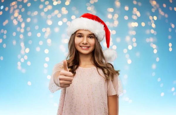 Felice ragazza adolescente in cappello di Babbo Natale mostrando pollici in su — Foto Stock