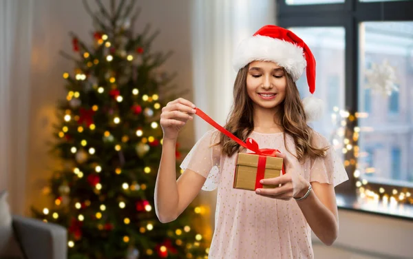 Dospívající dívka v Santa klobouk otevření vánoční dárek — Stock fotografie