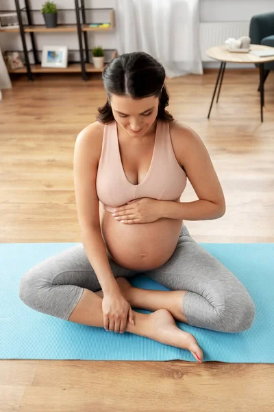 Happy pregnant woman sitting on yoga mat at home — Stock Photo, Image