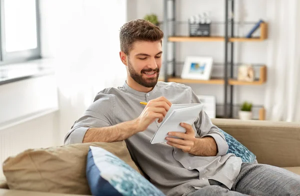 Homme souriant écrivant au carnet à la maison — Photo