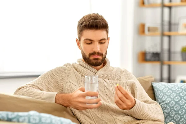 Zieke man met glas water en medicijnen thuis — Stockfoto