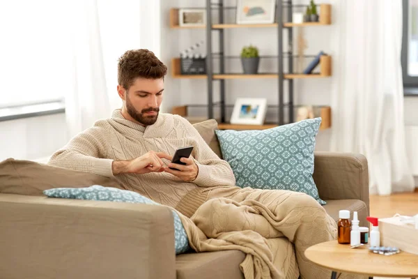 Joven enfermo en manta con teléfono inteligente en casa —  Fotos de Stock