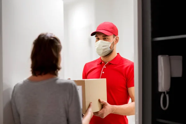 Homem da entrega na máscara que dá a caixa do pacote ao cliente — Fotografia de Stock