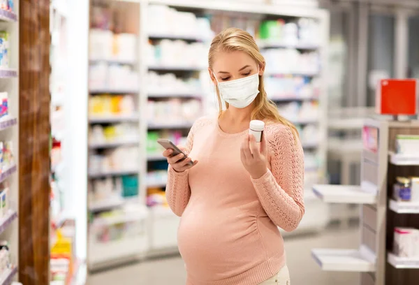 Mulher grávida em máscara com a medicina na farmácia — Fotografia de Stock