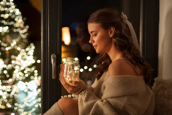 Mulher com luzes de grinalda de Natal em caneca de vidro — Fotografia de Stock