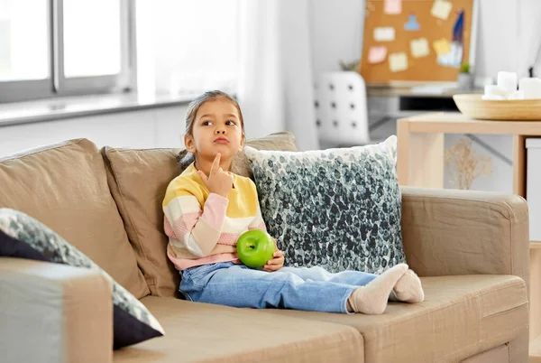 Liten flicka med äpple sitter på soffan — Stockfoto