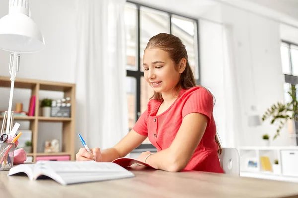 Estudiante chica con libro de escritura a cuaderno en casa — Foto de Stock