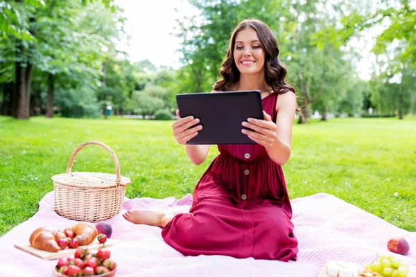 Mujer feliz con la tableta en el picnic en el parque —  Fotos de Stock