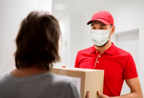 Homem da entrega na máscara que dá a caixa do pacote ao cliente — Fotografia de Stock