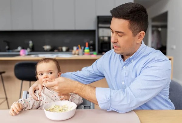 Отец среднего возраста кормит дочку дома — стоковое фото