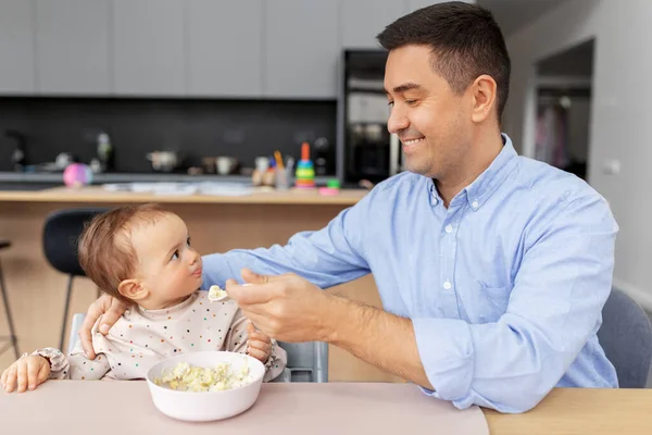 Glücklicher Vater füttert Baby im Hochstuhl zu Hause — Stockfoto
