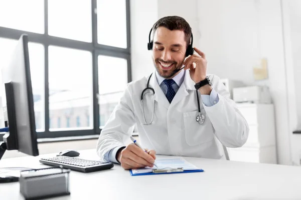 Glad läkare med dator och headset på sjukhus — Stockfoto