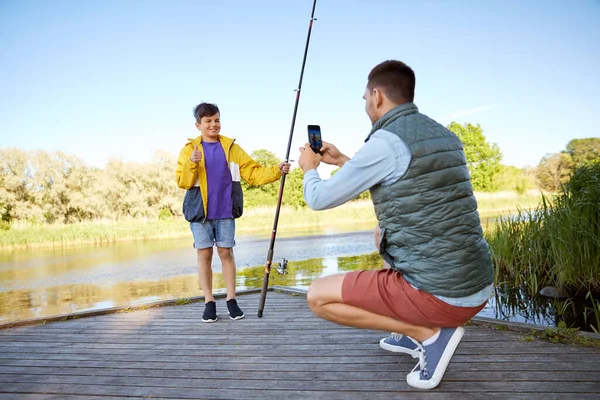 Pai fotografando filho com vara de pesca no rio — Fotografia de Stock