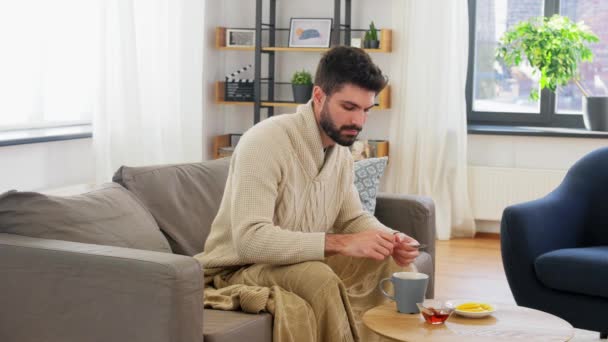 Sick young man in blanket drinking hot tea at home — Stock Video