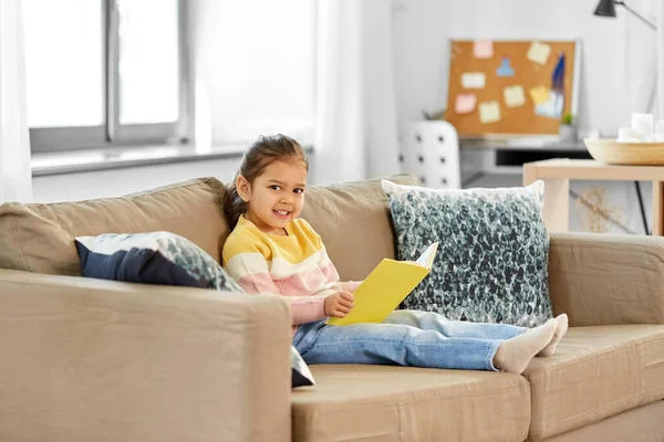 Glad leende liten flicka läsa bok hemma — Stockfoto