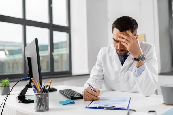 Gestresster Arzt mit Klemmbrett im Krankenhaus — Stockfoto