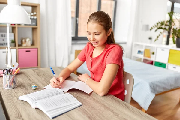 Student flicka med bok skriva till anteckningsbok hemma — Stockfoto