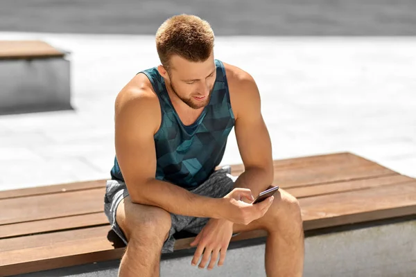 Man with smartphone sitting on bench outdoors — Stock Photo, Image