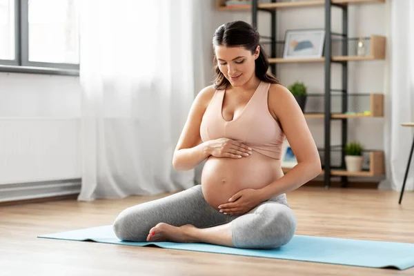 Šťastná těhotná žena sedí doma na podložce na jógu — Stock fotografie