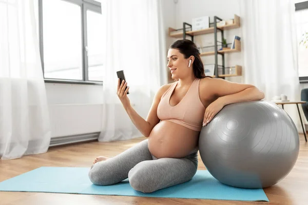 Terhes nő okostelefonnal és fitball otthon — Stock Fotó