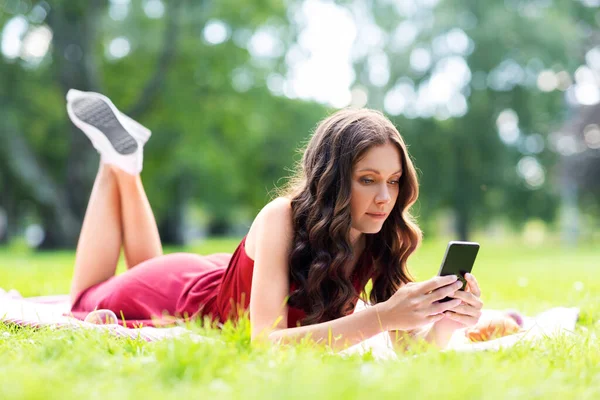 Krásná mladá žena s chytrým telefonem v parku — Stock fotografie