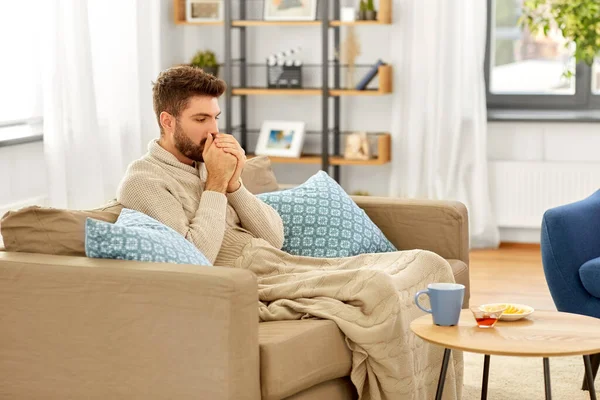 Хворий молодий чоловік в ковдрі з гарячим чаєм вдома — стокове фото