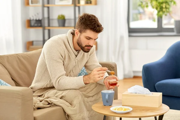Больной молодой человек в одеяле пьет горячий чай дома — стоковое фото