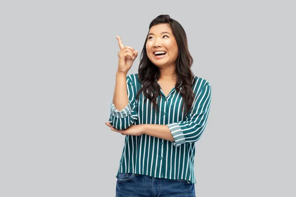 Heureux asiatique femme pointant doigt jusqu 'sur gris — Photo