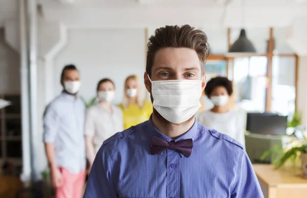 Young man in mask over creative team at office — Stock Photo, Image