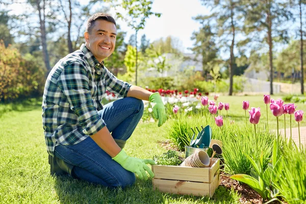Homme heureux avec des outils dans la boîte et des fleurs au jardin — Photo
