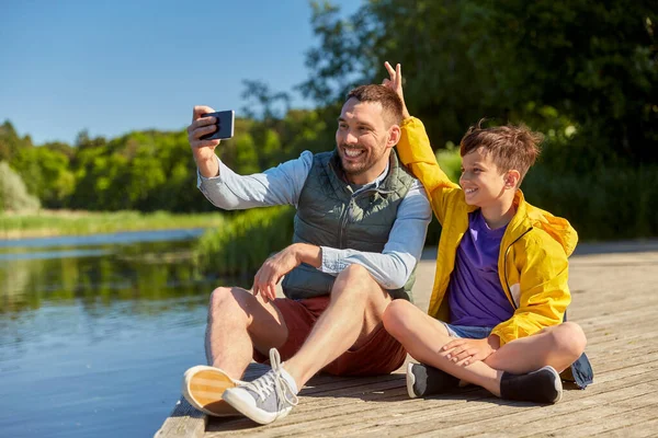 Baba ve oğul nehirde telefonla selfie çekiyorlar. — Stok fotoğraf