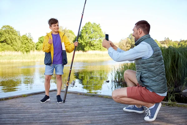 Pai fotografando filho com vara de pesca no rio — Fotografia de Stock