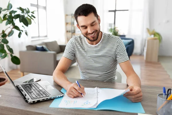 Man met papieren en laptop die thuis werkt — Stockfoto