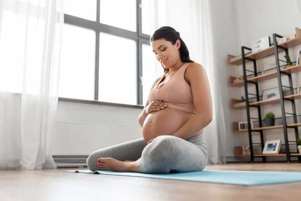 Happy pregnant woman sitting on yoga mat at home — Stock Photo, Image