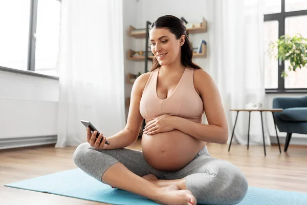 Heureuse femme enceinte avec téléphone faire du yoga à la maison — Photo