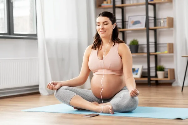 Zwanger vrouw met koptelefoon mediteren thuis — Stockfoto