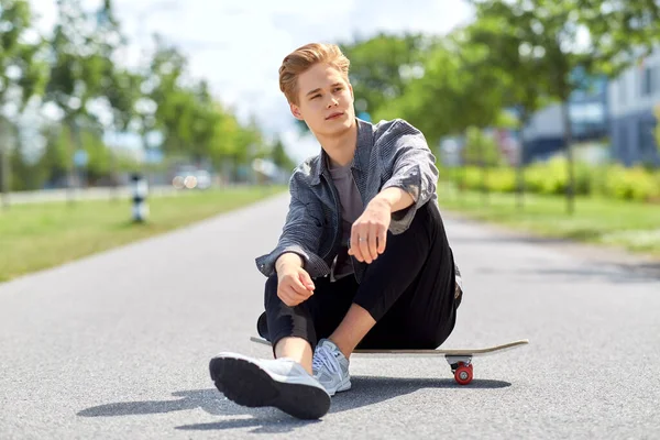 Έφηβος αγόρι κάθεται στο skateboard στην πόλη δρόμο — Φωτογραφία Αρχείου