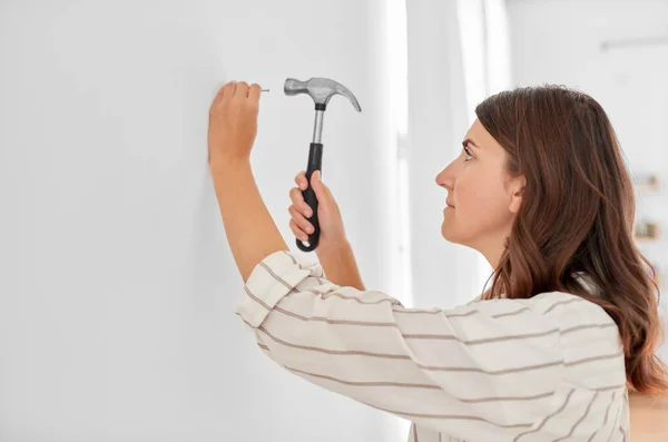 Mulher martelando unha a parede em casa — Fotografia de Stock