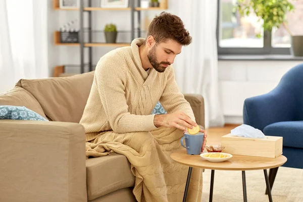 Больной молодой человек в одеяле пьет горячий чай дома — стоковое фото